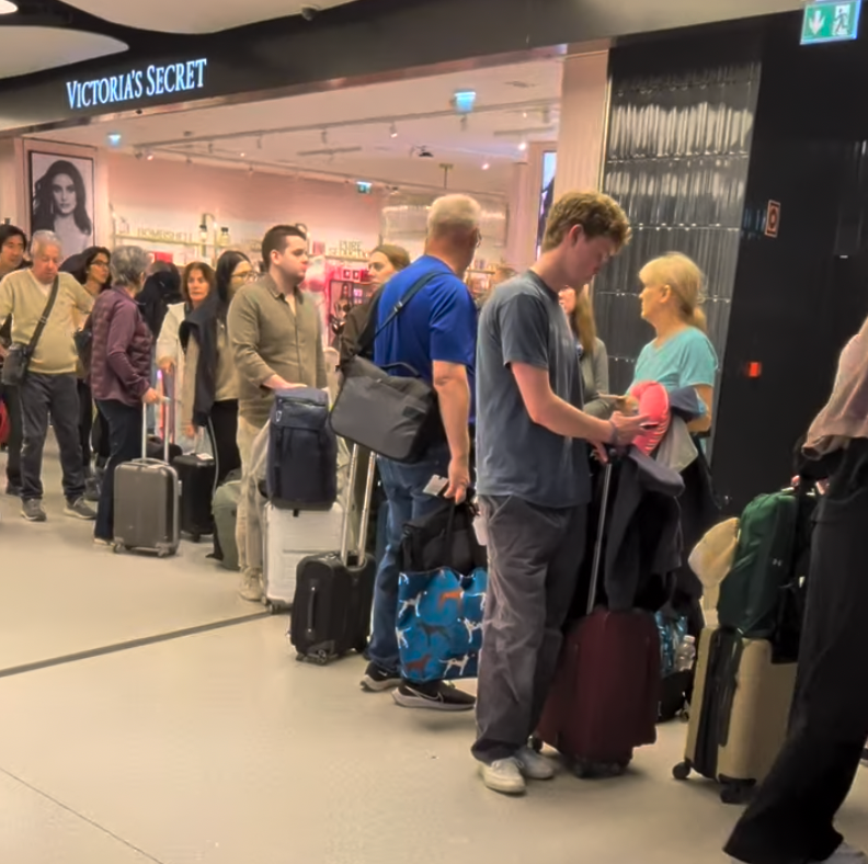 Long passport control queue at Lisbon Airport with American travellers and luggage near a Victoria's Secret store